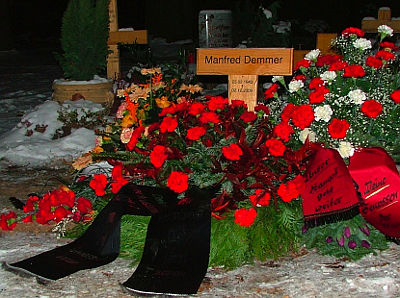 Blumen am Grab und schwarze und rote Schleife. Tafel: Manfred Demmer ∗ 25.02.1943  † 02.12.2009